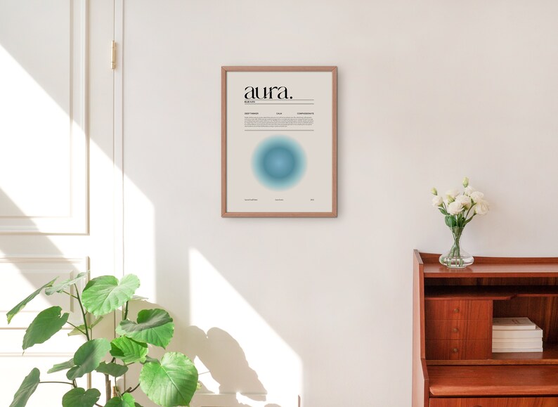 May include: A framed print with the word "aura" in black text on a white background. The print features a blue and green gradient circle in the center. The print is hanging on a white wall.