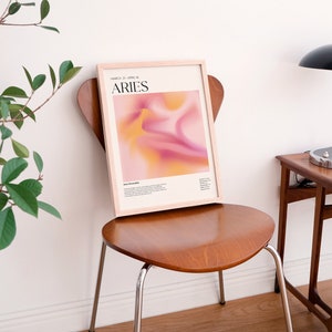 May include: A framed print with a pink and orange abstract design. The print has the text "March 21 - April 19" and "Aries" in black text.
