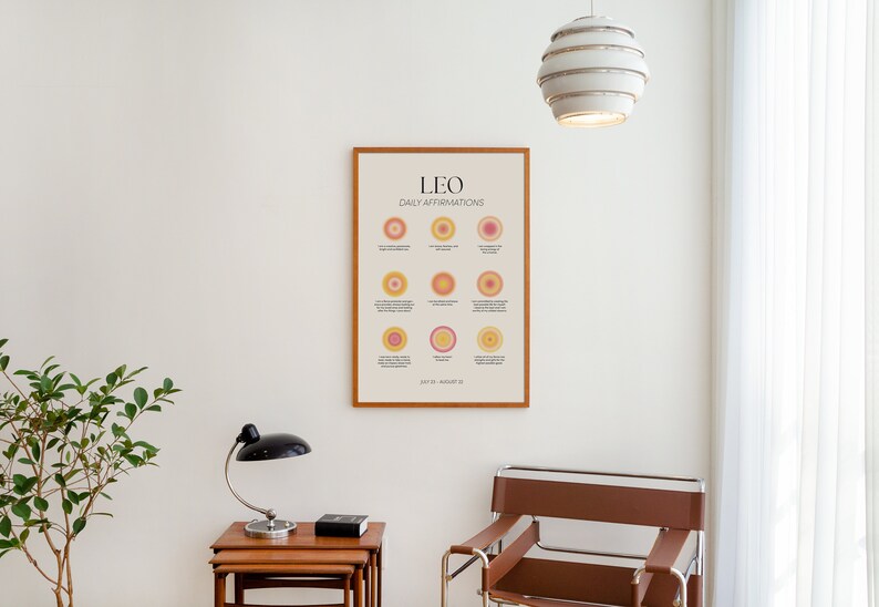 May include: A framed print with the text "LEO DAILY AFFIRMATIONS" and a series of colorful circles. The print is hanging on a white wall in a room with a brown chair and a lamp.