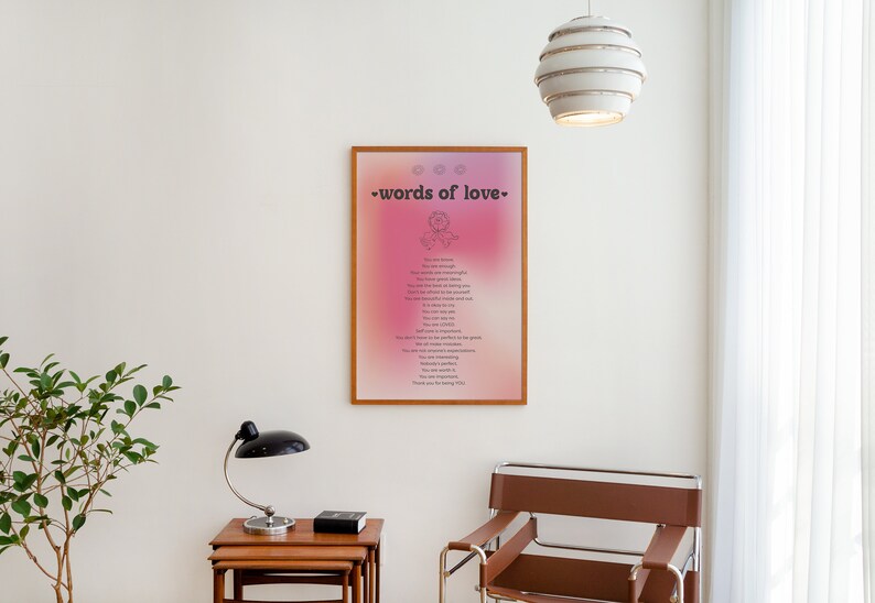 Pode incluir: Uma impress&atilde;o emoldurada com um fundo degrad&ecirc; rosa e roxo. A impress&atilde;o apresenta o texto "words of love" e uma pequena ilustra&ccedil;&atilde;o de um cora&ccedil;&atilde;o com uma flor dentro. A impress&atilde;o est&aacute; pendurada em uma parede branca em um quarto com uma cadeira marrom e uma pequena planta.