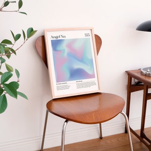 May include: A framed print with a light blue, pink, and purple abstract design. The print has the text "Angel No. 555" at the top. The print is sitting on a wooden chair in front of a white wall.