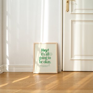 May include: A framed print with a white background and green text that reads "Hey! It's all going to be okay."  A green smiley face is next to the text.