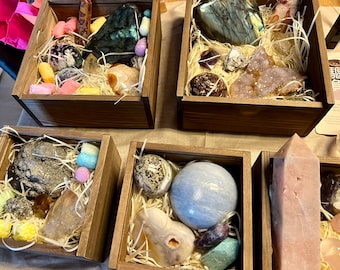 May include: Assortment of crystals and stones in wooden boxes. The boxes are filled with straw and the crystals are arranged in a variety of colors and shapes. Some of the crystals are polished and others are rough.