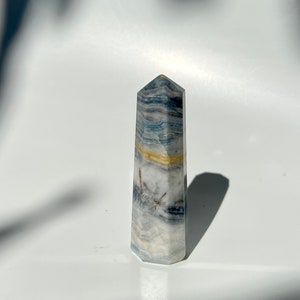 Könnte beinhalten: Eine blaue und weiße gebänderte Kristallspitze mit goldenen Akzenten. Der Kristall ist poliert und hat eine spitze Spitze.