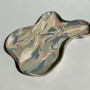 May include: A ceramic tray with an abstract marbled design in shades of green, blue, pink, and white. The tray has an irregular, organic shape.