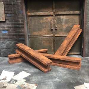 Könnte beinhalten: Drei rostige Metallbalken, die übereinander gestapelt sind. Die Balken sind braun und haben eine raue Textur. Sie liegen auf einer Betonfläche.