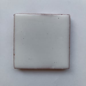 May include: A white ceramic tile with a slightly rough texture and a subtle pink border.