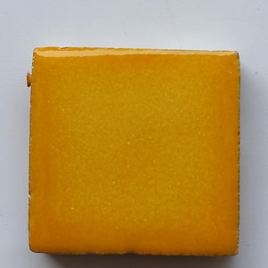 May include: A square ceramic tile with a bright yellow glaze.