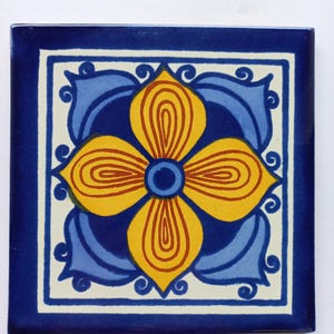 May include: A blue and white ceramic tile with a yellow flower design. The flower has a blue center and is surrounded by blue and white swirls.
