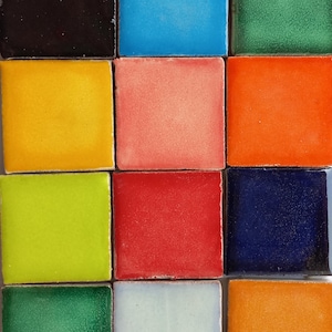 Puede incluir: Un conjunto de 12 azulejos de cerámica en varios colores, incluyendo negro, azul, amarillo, rosa, verde, rojo, azul marino, blanco y naranja. Los azulejos están dispuestos en un patrón de cuadrícula.