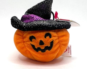 May include: Orange plush pumpkin with a black witch hat with purple glitter. The pumpkin has a black stitched-on face with a wide smile and eyes. The tag reads "Scream" and "Handmade in China."