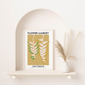 K&ouml;nnte beinhalten: Ein gerahmter Druck mit einem minimalistischen Design, das eine stilisierte Illustration einer rosa und gr&uuml;nen Blume auf gelbem Hintergrund zeigt. Der Text "FLOWER MARKET" und "S&Atilde;O PAULO" ist in Schwarz gedruckt.