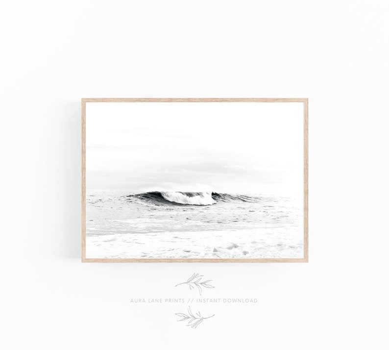 May include: Black and white photograph of a wave crashing in the ocean. The wave is breaking in the foreground, with the horizon in the background.