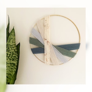 May include: A circular wall hanging with a gold metal hoop and colourful yarn woven in a geometric pattern. The yarn is in shades of blue, green, and white.