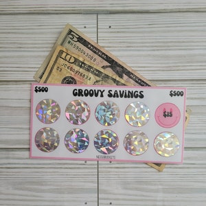 May include: A pink and white card with the text "GROOVY SAVINGS" and a grid of nine iridescent stickers. Each sticker is a circle with a holographic design. The card also has the text "$500" on the top left and right corners. The text "$15" is on a sticker in the top right corner.