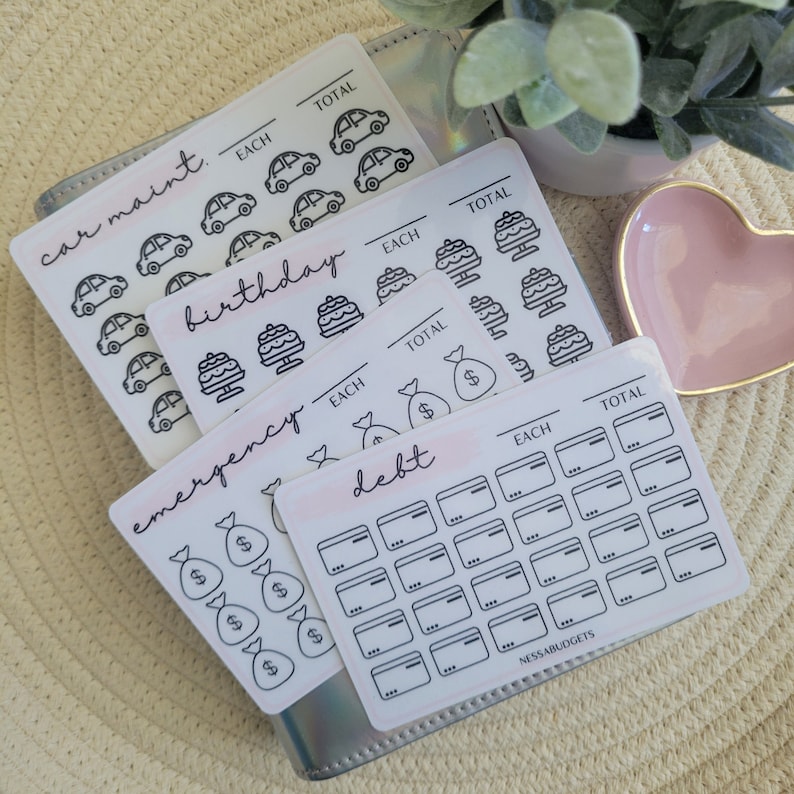 May include: A set of printable stickers for budgeting and tracking expenses. The stickers feature icons for car maintenance, birthday, emergency fund, and debt. Each sticker has a section for "each" and "total" amounts.