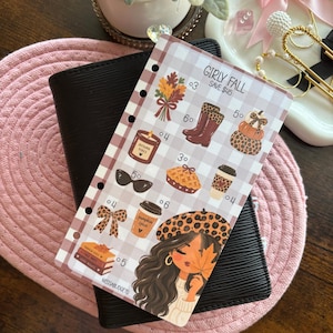 May include: A rectangular planner insert with a light brown and white gingham pattern featuring the text GIRLY FALL and SAVE $45. It displays illustrations of autumn leaves, boots, pumpkins, a candle, sunglasses, pie, coffee, a bow, and a person.