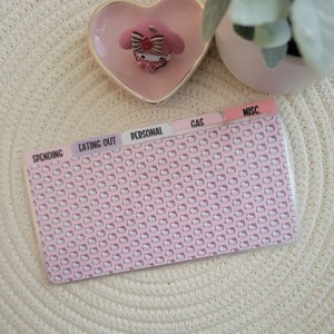 May include: Pink Hello Kitty themed budget binder with dividers labelled "Spending", "Eating Out", "Personal", "Gas", and "Misc."