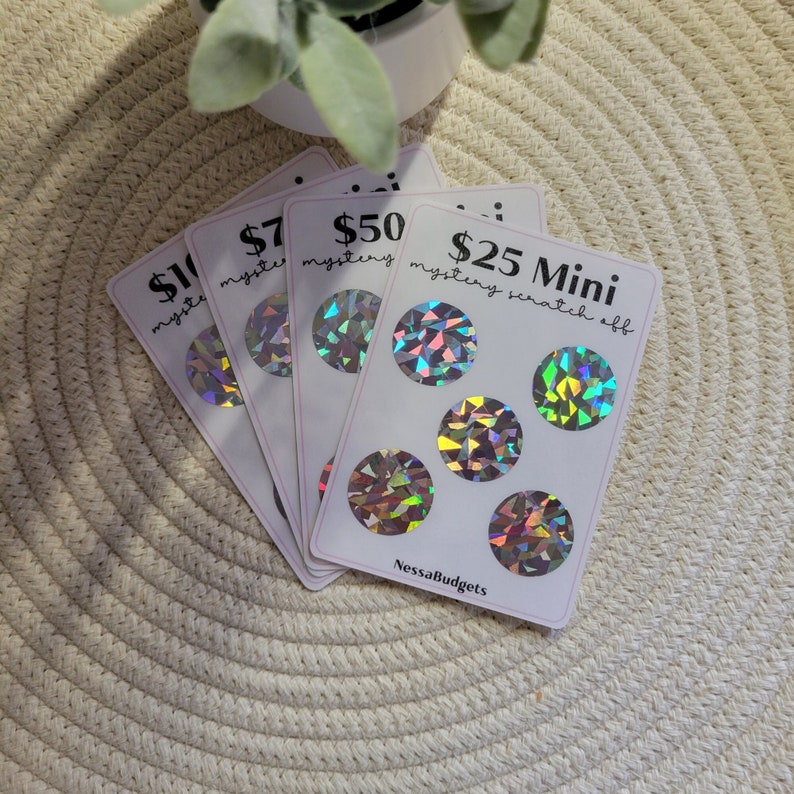 May include: Four scratch-off cards with holographic foil designs. The cards are labeled with dollar amounts: $10, $7, $50, and $25 Mini mystery scratch off. The cards are on a white surface.