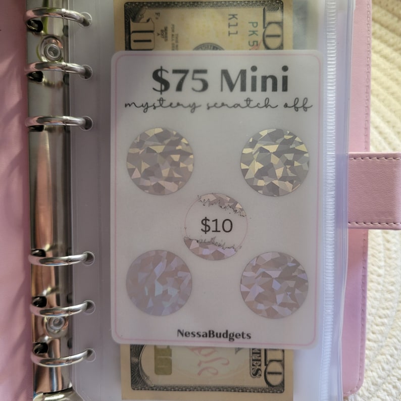 May include: A white card with the text "$75 Mini mystery scratch off" and four silver scratch-off circles. The card also has the text "$10" and "NessaBudgets".