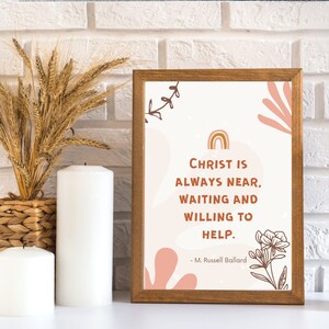 May include: A framed print with a pink background and a quote that reads "Christ is always near, waiting and willing to help." The quote is attributed to M. Russell Ballard. The print has a rainbow and floral illustrations.