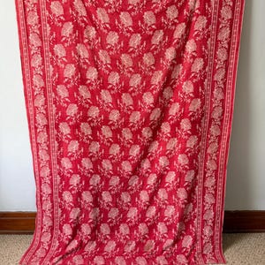 May include: A rectangular textile featuring a vibrant red background with a repeating cream-coloured floral pattern. The fabric displays a central field of scattered flower motifs framed by two vertical borders containing a dense floral vine design.