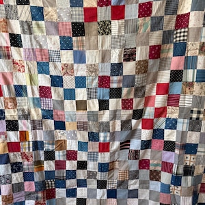 May include: A patchwork quilt composed of numerous small square fabric pieces in a variety of colors and patterns, including red, blue, white, black, and grey, featuring diverse textures like gingham, stripes, florals, and solid colors.