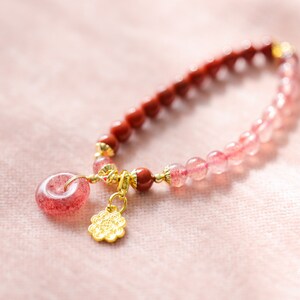 May include: A pink and red gemstone bracelet with a gold charm. The bracelet is made of small, round beads and has a delicate, feminine look.