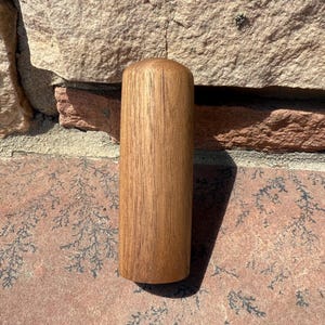 May include: A cylindrical wooden object with a rounded top. The wood grain is visible, and the color is a warm brown. The object is standing upright against a brick wall.