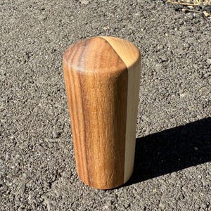 May include: A handcrafted wooden tumbler with a conical top and a cylindrical body. The tumbler is made of two types of wood, with a light-colored wood section on one side and a darker wood on the other. The tumbler is approximately 5 inches tall.