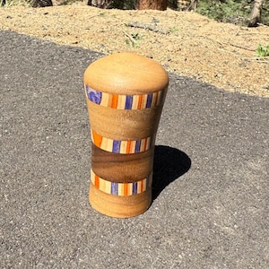 May include: A handcrafted wooden bottle stopper with a rounded top. The stopper features bands of alternating colours: orange, blue, and natural wood. The stopper is approximately 10 cm tall.