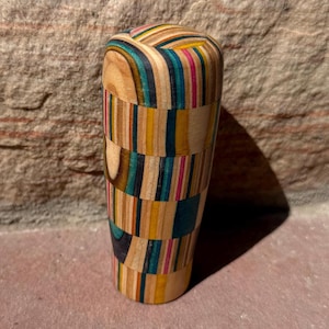 May include: A handcrafted wooden tumbler with a unique design. The tumbler is made from various colorful wood strips, including shades of blue, pink, yellow, and natural wood tones. The tumbler is approximately 13 cm tall.