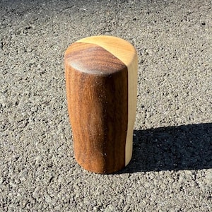 May include: A cylindrical wooden object, likely a decorative item. The top is light brown, split into two sections. The sides are a darker brown, creating a two-tone effect. The object's design suggests it could be a small stool or a decorative piece.