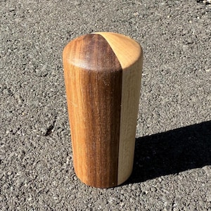May include: A cylindrical wooden object with a rounded top. The top is divided into two sections, one dark brown and the other light brown. The body is vertically split into a dark and light brown section.