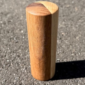 May include: A wooden bottle stopper with a cylindrical shape. The top is a light brown colour, divided into two sections. The body is a lighter shade of brown. The stopper is made of wood and has a smooth finish.