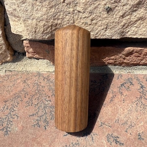 May include: A solid, cylindrical wooden candle with a pointed top. The candle is a warm brown color, showcasing the natural wood grain. It stands approximately 6 inches tall and is unlit, suggesting it's for decorative use.