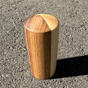 May include: A cylindrical wooden knob, likely for a cabinet or drawer. The knob is made from two types of wood, one light and one darker. The knob's design features a contrasting colour scheme, with a light and dark section.