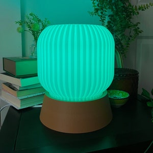 May include: A green and brown table lamp with a ribbed, cylindrical shade and a round base. The lamp is lit and casting a green glow.