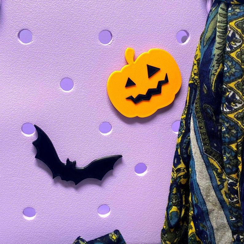 May include: A purple pegboard with a black bat, an orange pumpkin, and a blue and yellow patterned scarf.
