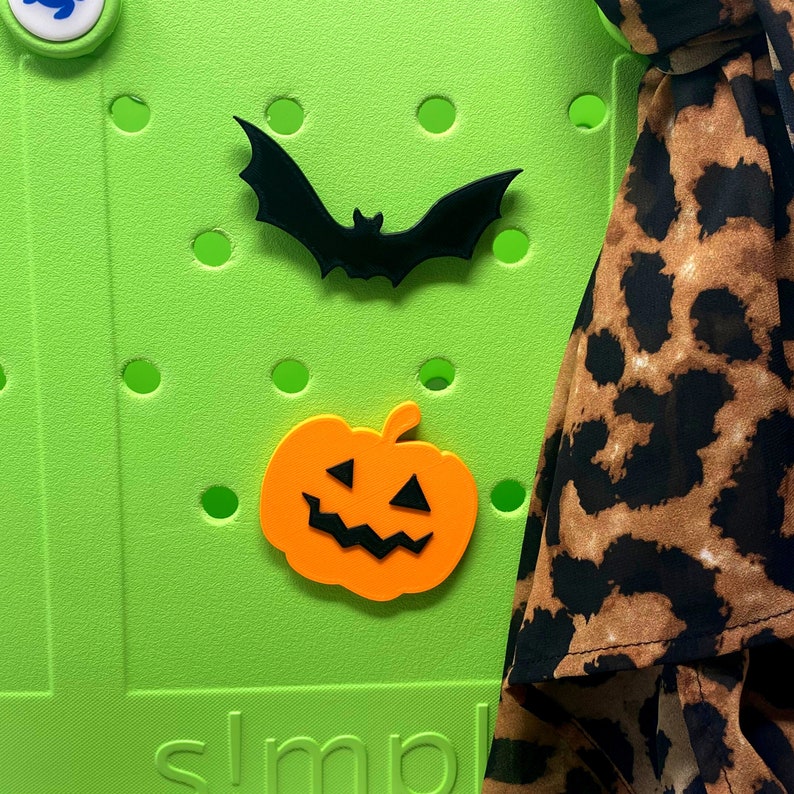 May include: A green pegboard with a black bat and an orange pumpkin cutout. The pegboard has the word "simple" written on the bottom. A brown and black leopard print scarf is on the right side of the image.