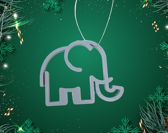 Pode incluir: Um enfeite de elefante prateado com um laço de corda para pendurar. O enfeite está sobre um fundo verde com flocos de neve brancos e glitter dourado.