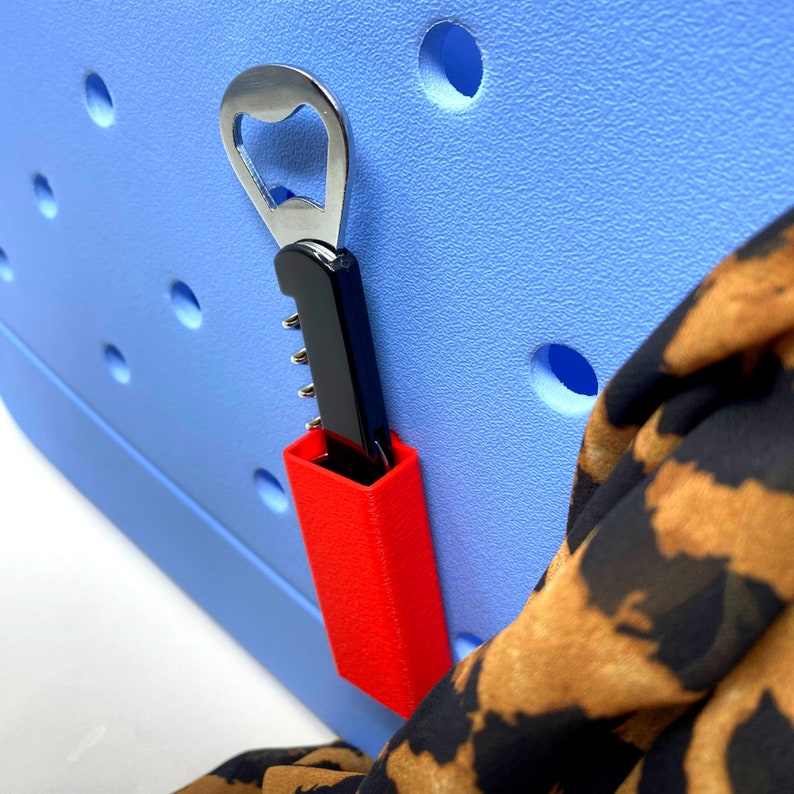May include: A red and black bottle opener with a corkscrew attached. The opener is attached to a blue cooler with a pattern of circles.
