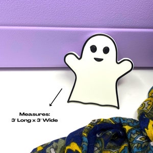 May include: White ghost-shaped Halloween decoration with black outline and eyes. Measures 3 inches long by 3 inches wide.
