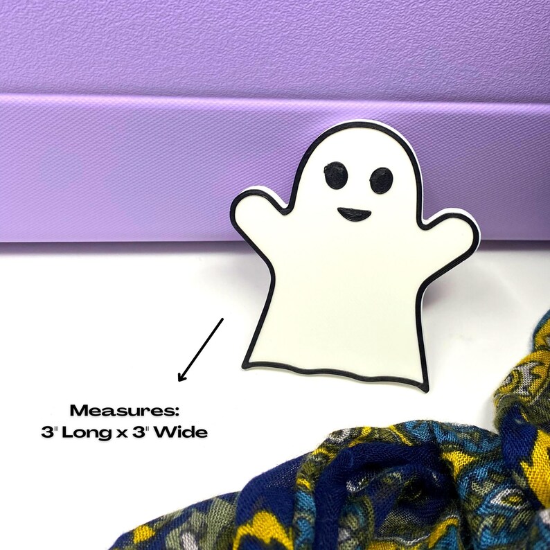 May include: White ghost-shaped Halloween decoration with black outline and eyes. Measures 3 inches long by 3 inches wide.