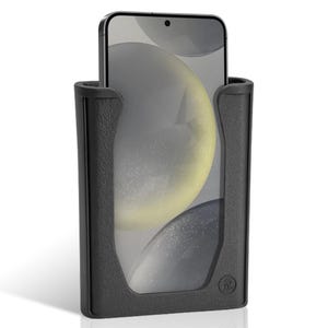K&ouml;nnte beinhalten: Ein schwarzer Telefonhalter mit strukturierter Oberfl&auml;che, der ein Smartphone h&auml;lt. Der Bildschirm des Telefons zeigt ein verschwommenes, abstraktes Design mit Gelb- und Graut&ouml;nen. Der Halter hat einen abgerundeten Boden und ein Logo.