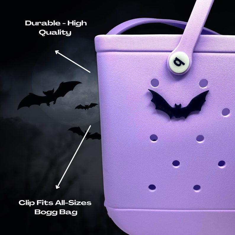 May include: A purple Bogg Bag with a black bat charm and a white clip with the letter "B" on it. The bag has a textured surface with small holes. The text "Durable - High Quality" is visible in the top left corner of the image. The text "Clip Fits All-Sizes Bogg Bag" is visible in the bottom left corner of the image.