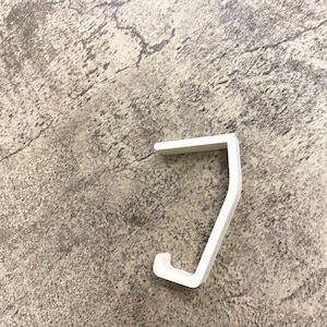 May include: White plastic hook for hanging items. The hook is shaped like a 'J' and has a smooth, rounded surface.