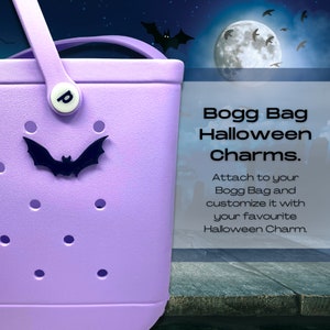 May include: Purple Bogg Bag with a black bat charm. The bag has a white handle and a white letter "p" on the front. The text "Bogg Bag Halloween Charms." is on a white background with a black border. The text says "Attach to your Bogg Bag and customize it with your favourite Halloween Charm."
