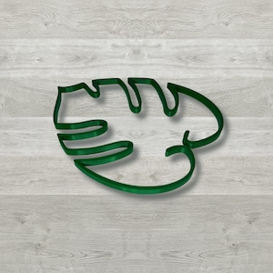 Pode incluir: Um contorno verde de uma folha de monstera em um fundo de madeira.