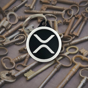 May include: A black and white keychain with the XLM logo on a white circle. The keychain is surrounded by a collection of old, rusty keys.